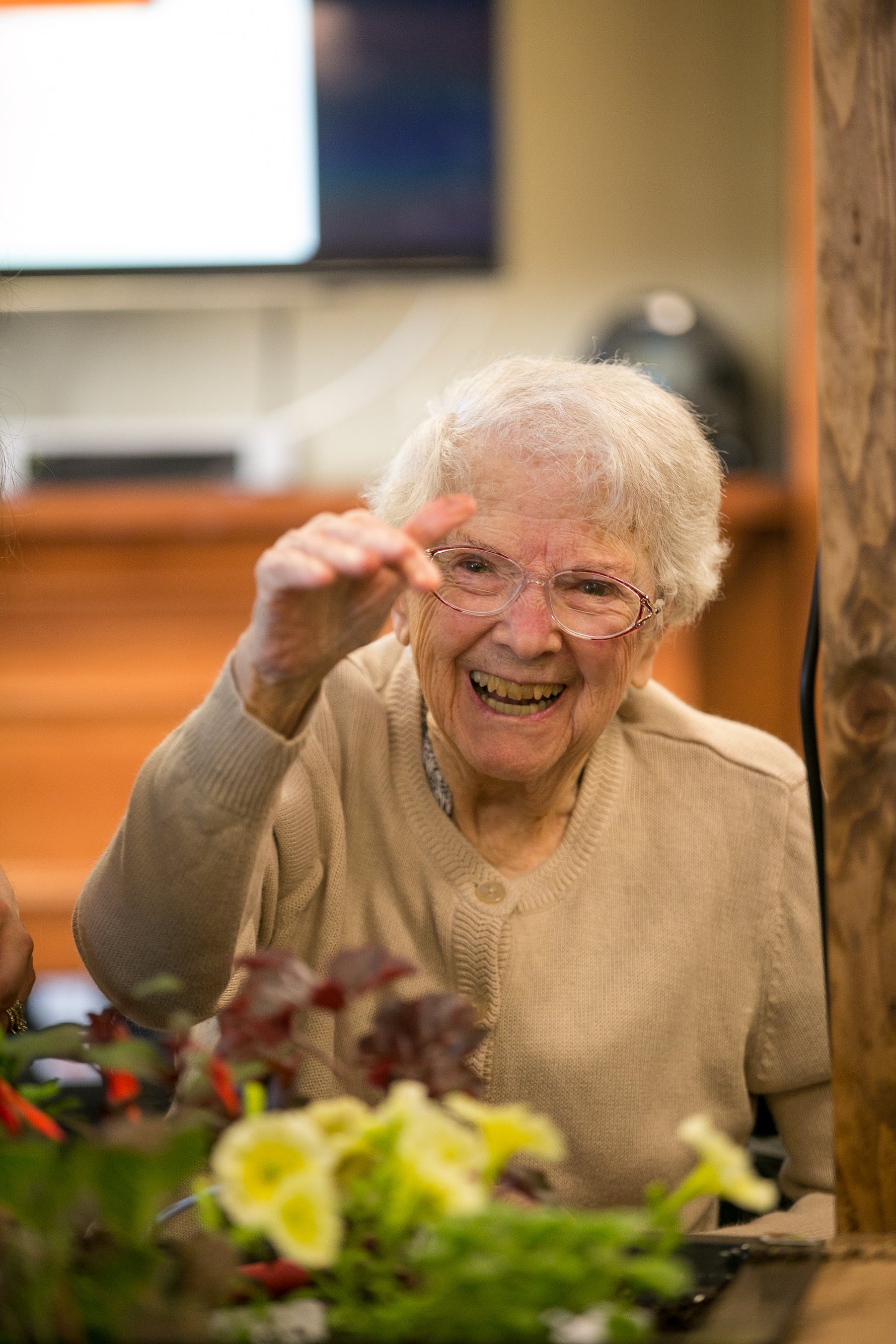 Senior woman smiling and pointing at a screen with a blurred indoor setting