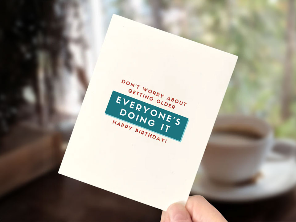 Hand holding the Birthday Card: ''Don't Worry about getting older, everyone's doing it'' written in red and turquoise.