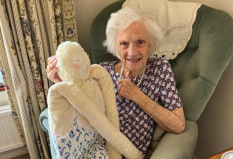Old woman sitting in a chair holding a HUG smiling.