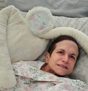 Person lying under a HUG dementia doll with a floral blanket