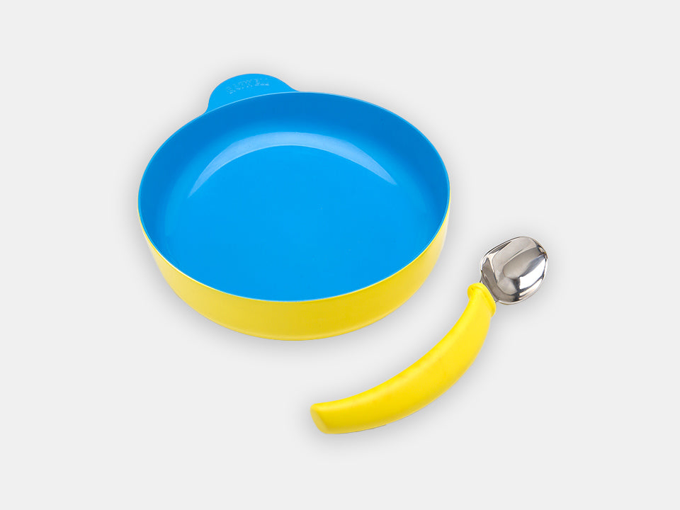 The yellow Ergonomically Curved Spoon from Eatwell next to an Eatwell bowl