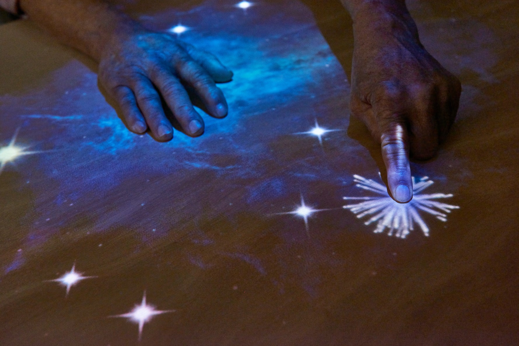 A close up of elderly hands playing and interacting with a Tovertafel game, with stars, being projected onto a table.