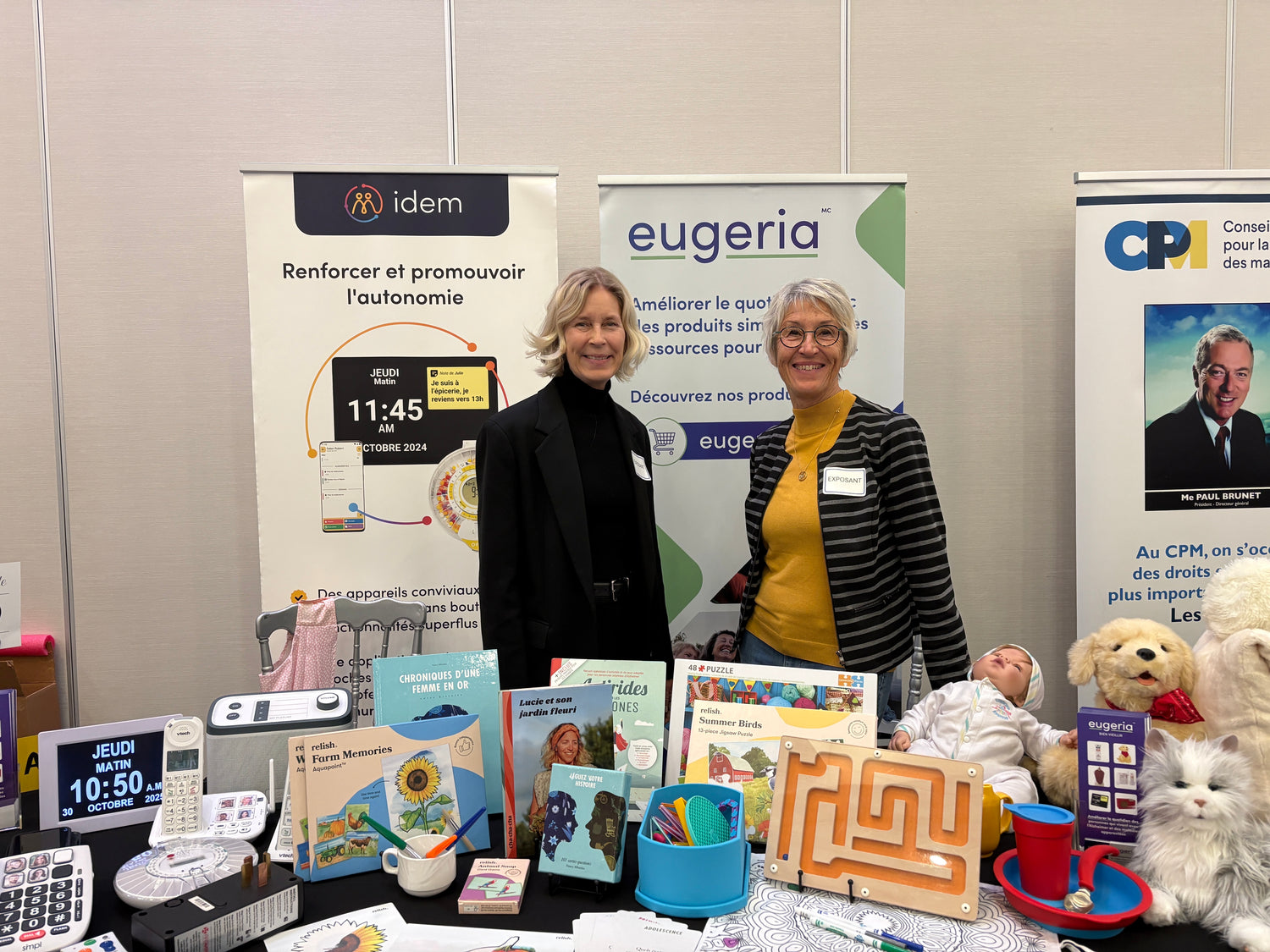 Two women standing behind a table with Eugeria's promotional materials and products at an event.