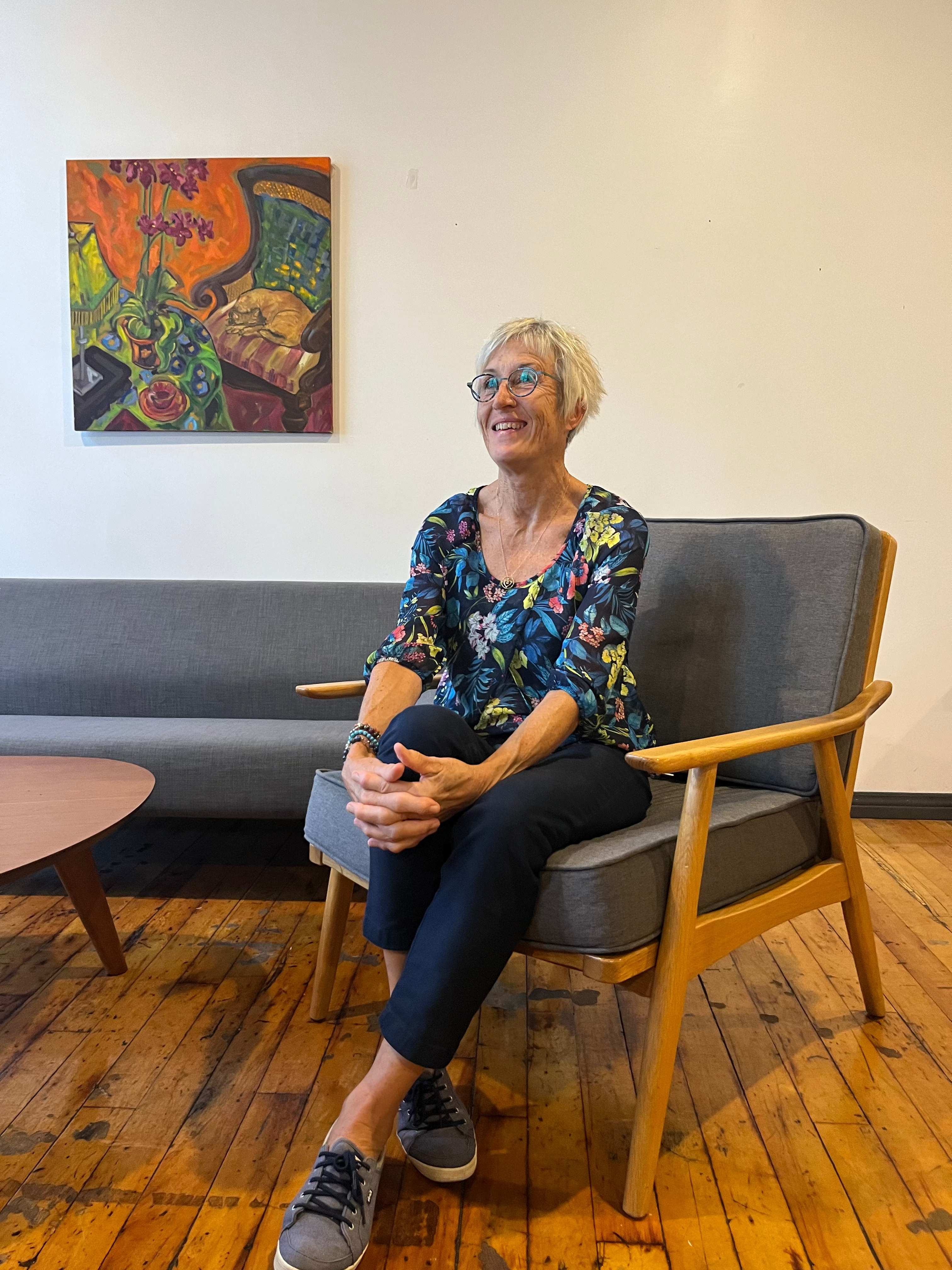 Woman sitting on a chair in a room with a colorful painting on the wall.
