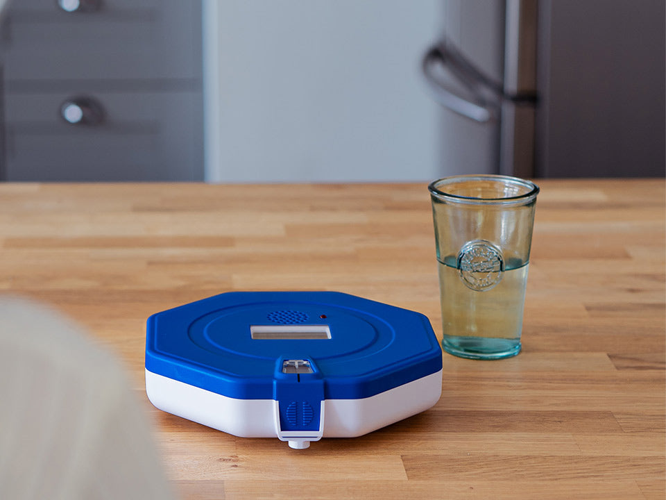 Pippa Tipper Lockable Pill Dispenser with a glass of water next to it 