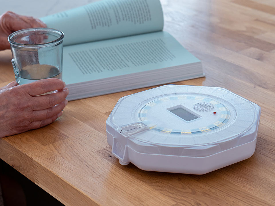 Someone reading a book next to the Pippa Tipper Lockable Pill Dispenser 