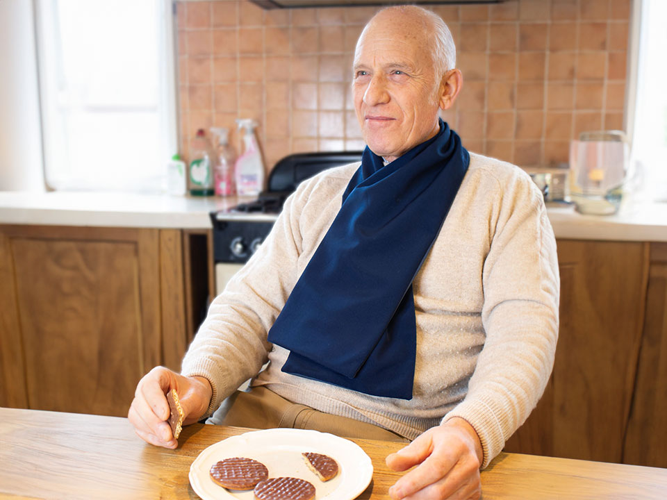 Older man in a kitchen eating while wearing the protective scarf bib in steel blue.