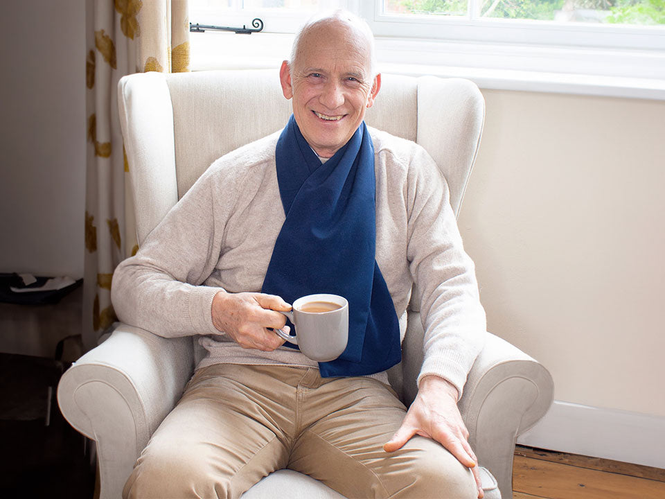 An older man drinking coffee on his living room couch while wearing the protective scarf bib.