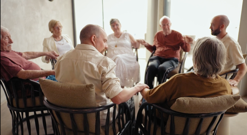 Group of elderly people sitting in a circle, holding hands during a Crdl interaction