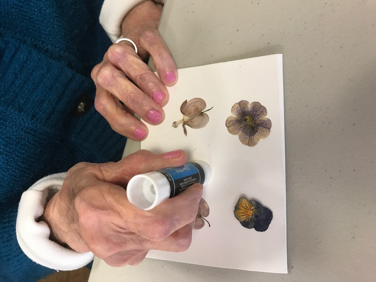 Person applying glue to pressed flowers on a piece of paper