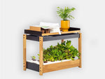 An indoor compact garden system featuring a wooden frame with black accents, equipped with a hydroponic growth bed and various plants either in pots or yet to sprout from the soil.

