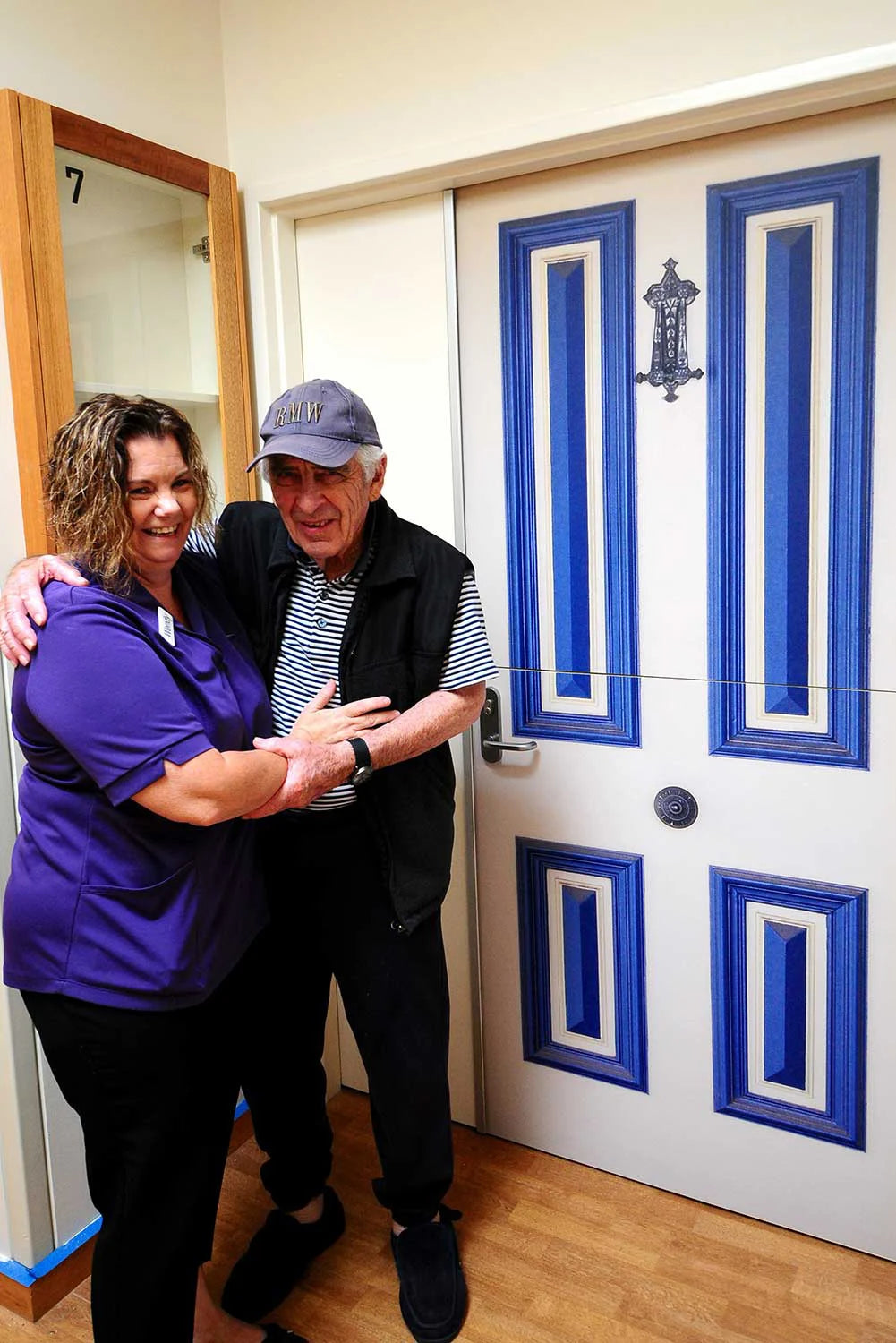 Two people posing in front of a True Doors white door with blue decorative panels.
