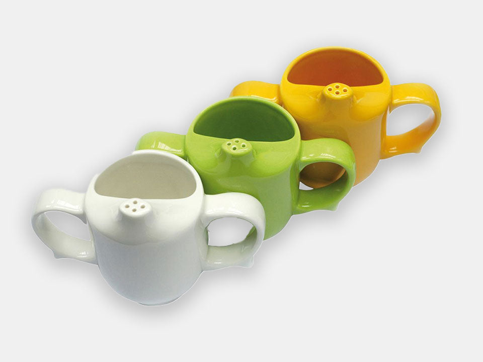 Angled top view of a white, a green, and a yellow mug, all designed to maintain dignity during mealtimes.
