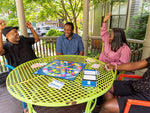 A group older adults smiling and playing Trivial Pursuit generations outside on their patio table.