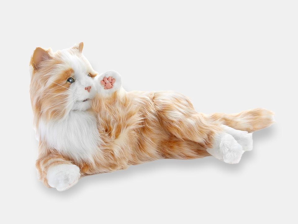 The orange companion cat designed for people living with dementia, on its side, with its paw lifted.