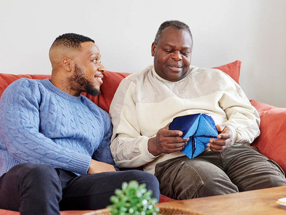 An elderly man with the Relish tactile-turn fidget toy designed for people living with dementia, sitting with his son.