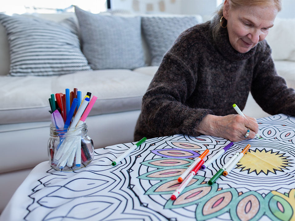 An older woman in her living room, coloring a bimoo mandala washable tablecloth.
