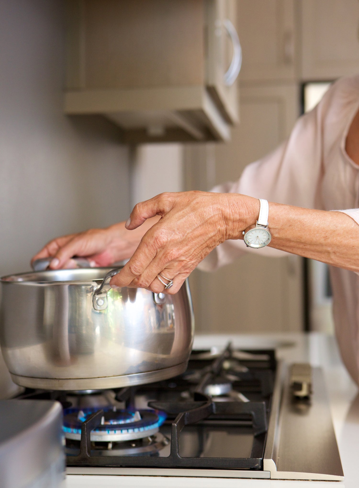 Elderly adult adjusting a pot on a gas stove in a kitchen