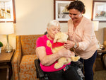 An older woman with her caregiver discovering and interacting with the golden pup by Ageless Innovation's.